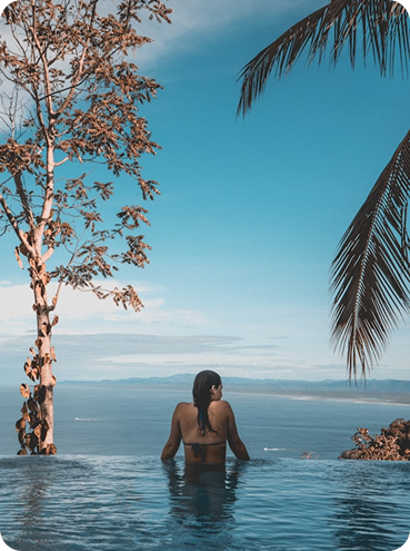 Mujer en piscina infinita contemplando el mar rodeada de naturaleza tropical, imagen representativa del estilo de vida exclusivo en Branded Residences.