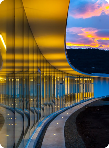 Fachada curva de edificio acristalado iluminado al atardecer, ejemplo de arquitectura contemporánea y diseño innovador en Branded Residences.